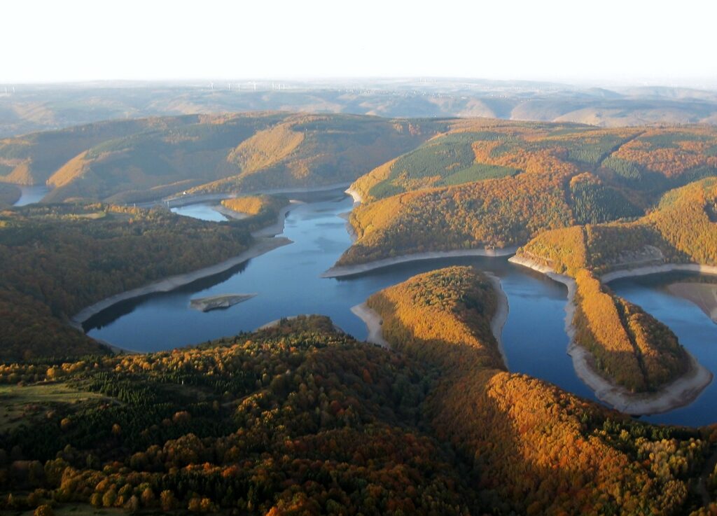 Luftaufnahme eines verschlungenen Gewässers im Herbst, das in orange-grüne Wälder eingebettet ist