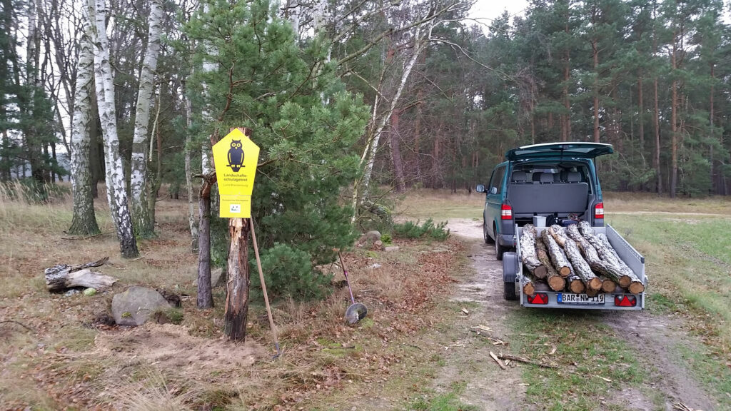 Zu sehen ist ein Landschaftsschutzgebiet-Schild mit FFH-Kennung, angebracht an einem Holzstamm am Waldrand.