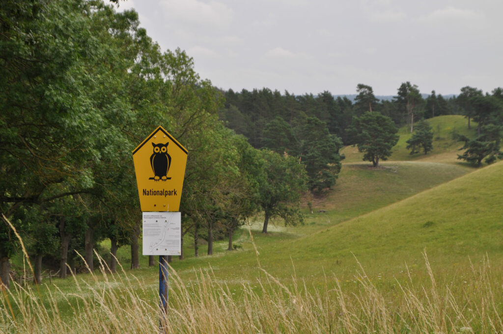 eine Wiese mit mit gelben Nationalpark-Schild mit Eule