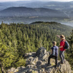 Zwei Wanderer genießen die Aussicht vom Falkenstein auf den umliegenden Wälder.