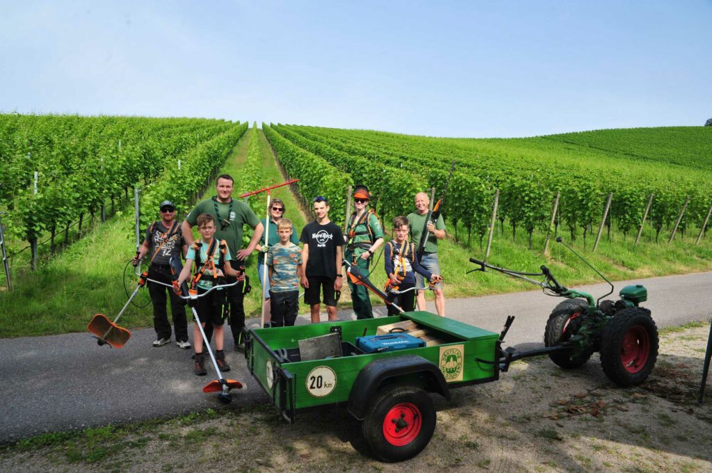 Eine Gruppe Kinder posiert vor einem gründen Feld mit kleinem Treckeranhänger und einem Erwachsenen.