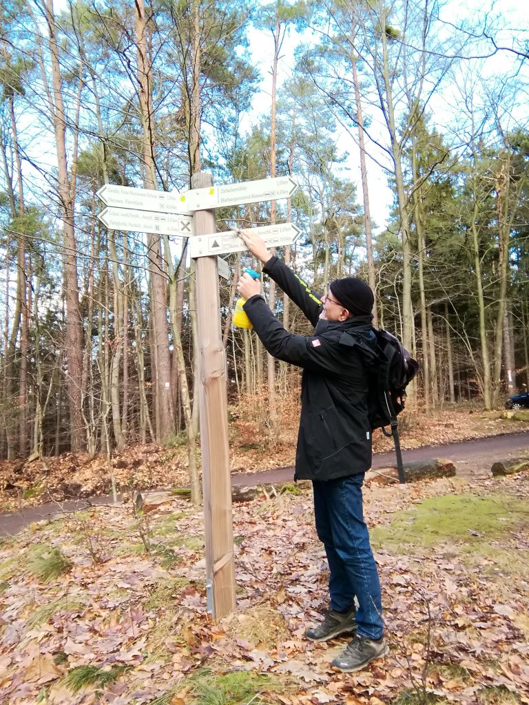 eine Person putzt die Schilder eines Wegweisers an einer Weggabelung