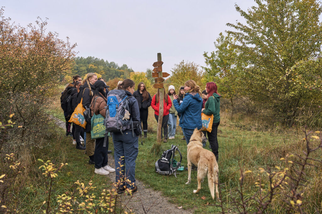 Eine Gruppe Menschen mit Hund steht zusammen um einen Wegweiser im Freien.
