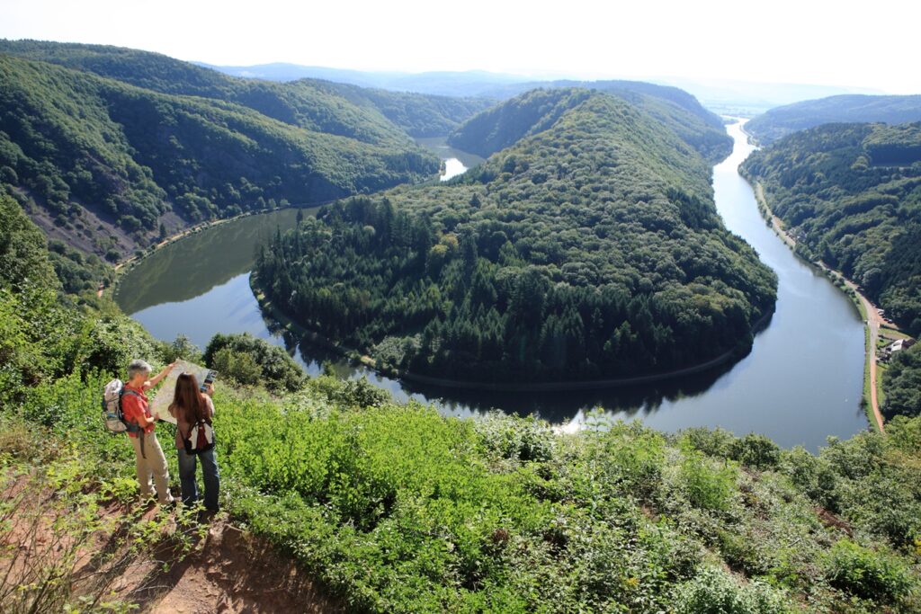 Zwei Wanderer lesen eine Karte. Im Hintergrund fließt die Saar und die grüne Landschaft steht im Vordergrund.