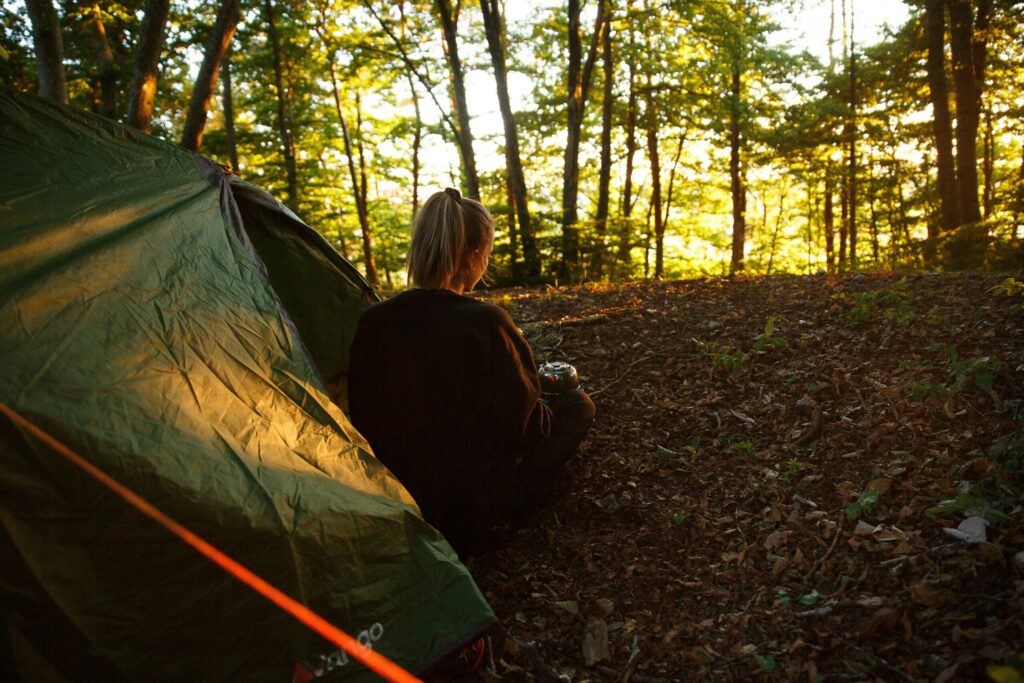 Eine Frau schaut aus einem Zelt heraus in einem Wald.