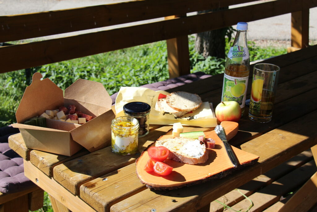 Ein hölzerner Tisch auf dem Apfelsaft, Brote, Gemüse und andere Lebensmitteln in Gläsern und Boxen stehen.