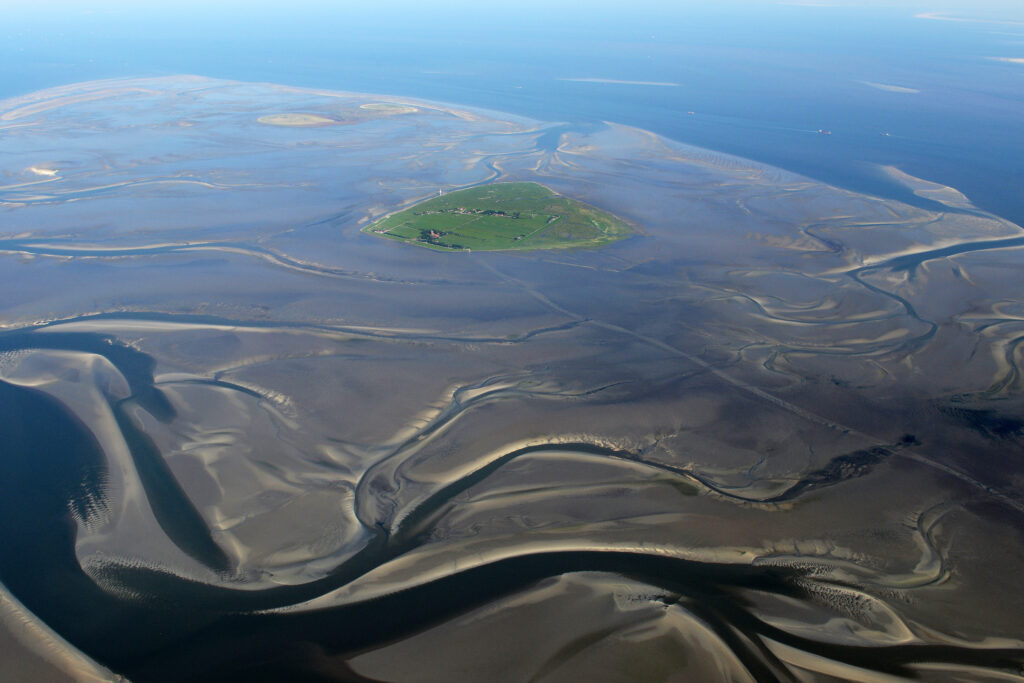 Luftaufnahme einer grünen, besiedelten Insel inmitten von Wasserläufen und Meer.