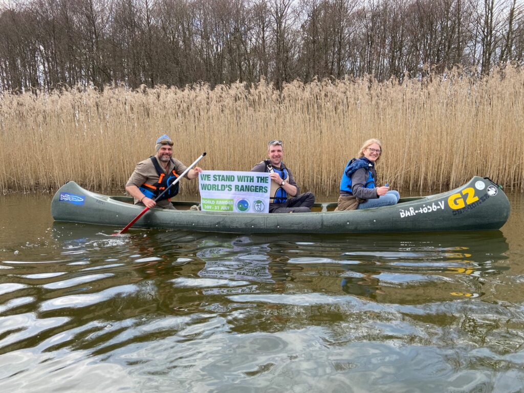 Drei Personen in einem Kanu präsentieren ein Banner mit dem Text "We stand with the world's rangers"