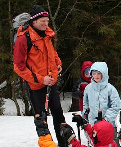 ein Mann in oranger Winterjacke und grauem Rucksack ist im Schnee unterwegs