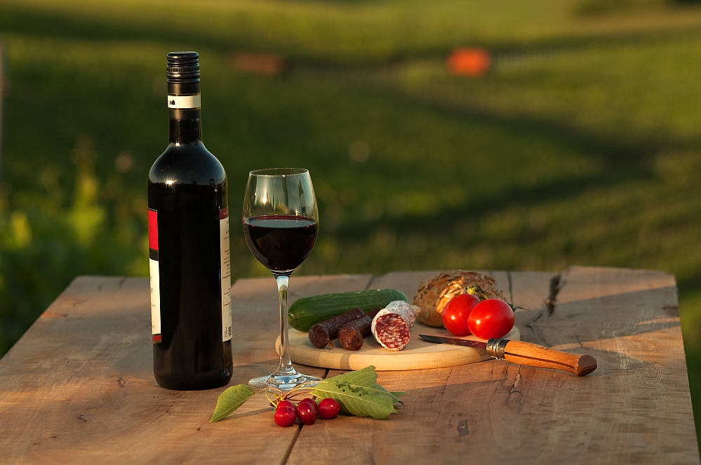 ein mit einer Flasche Rotwein und einem Brett mit Wurst, Kirschen und anderen lokalen Köstlichkeiten gedeckter Tisch in der Abendsonne