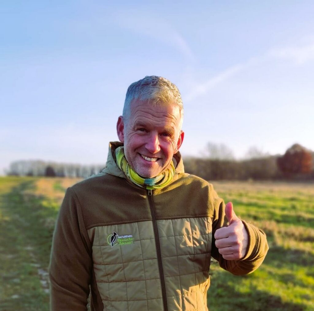 ein Mann mit grauem Haar lächelt in die Kamera und zeigt einen Daumen nach oben